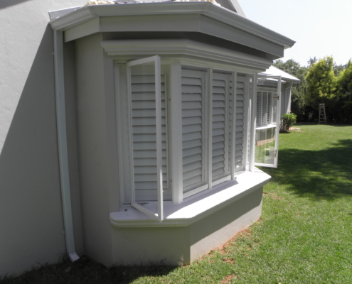 A white bay window featuring security shutters, showcasing a modern architectural design in a residential setting.